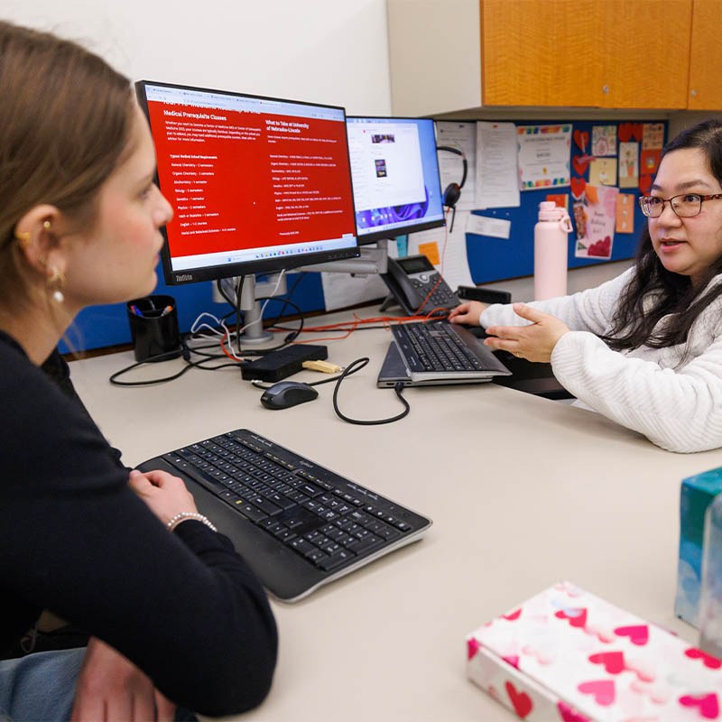 Two people sitting at a desk discussing information displayed on a computer screen.