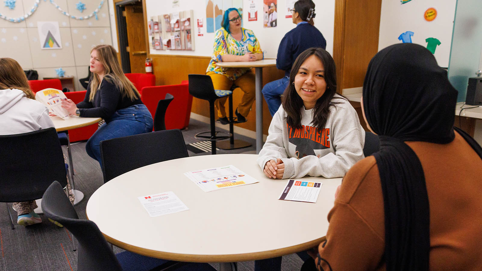 People conversing in a colorful indoor space with tables, chairs, and wall decorations.