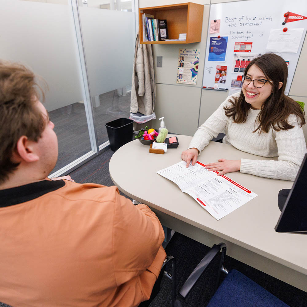Two people sitting at a desk in an office, discussing a document.